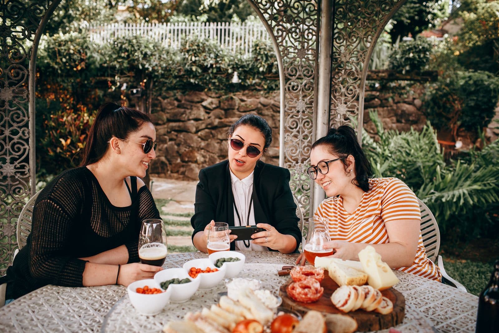 Three friends sharing drinks and snacks at a garden terrace table