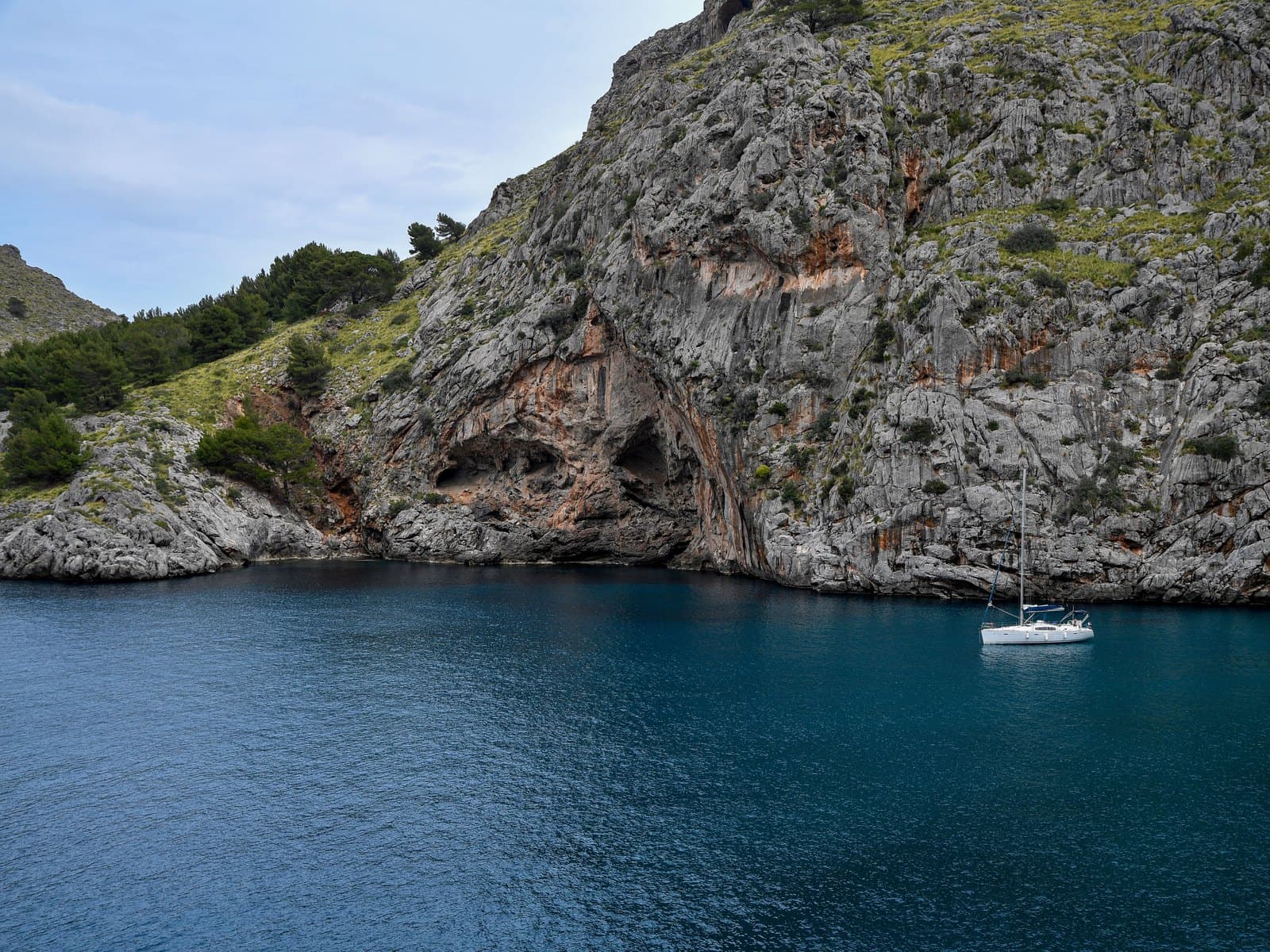A sailboat anchored below limestone cliffs in a Mallorcan cove