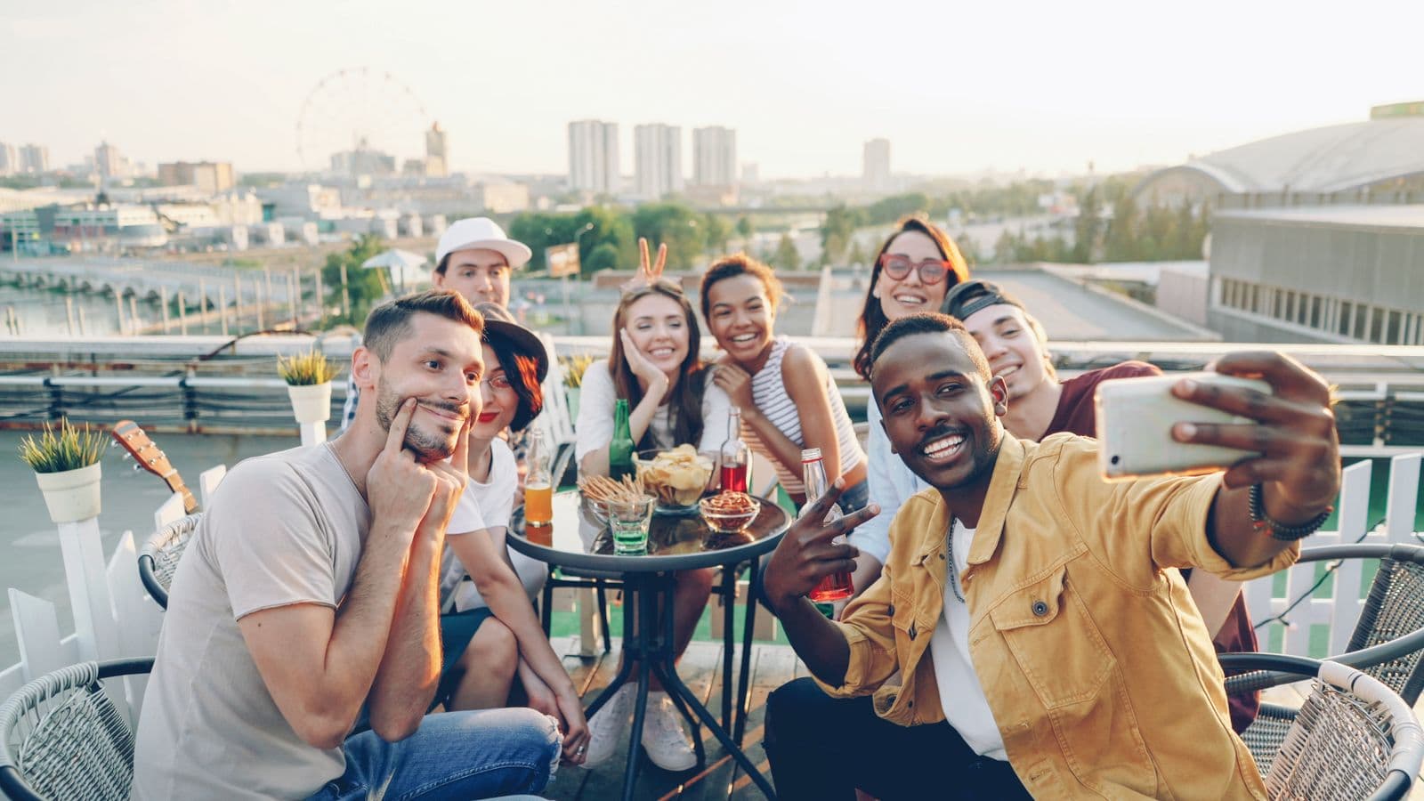 A group of friends taking a selfie around a rooftop table, city skyline behind them